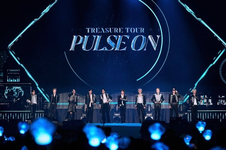 Grup K-Pop TREASURE tampil di atas panggung megah
             dalam konser Treasure Tour Pulse On, dengan tata
             cahaya biru neon dan layar LED besar di belakang mereka,
             disaksikan ribuan penonton yang memegang lightstick